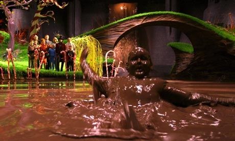 a group of people standing in water next to a fake waterfall with green plants on it