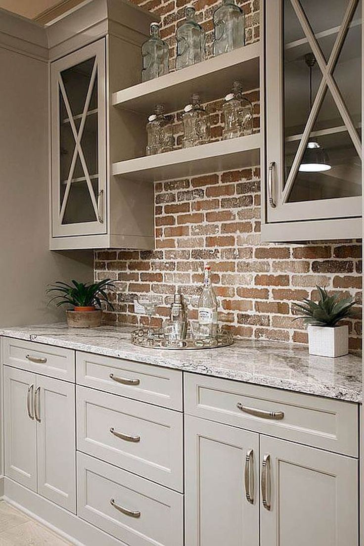 a kitchen with white cabinets and brick wall in the backround, filled with glassware