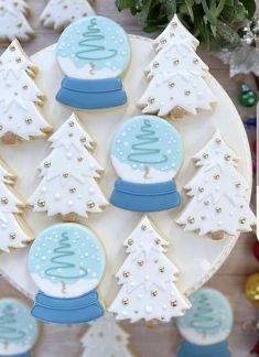 decorated cookies are displayed on a plate with christmas trees and snow globes in the background