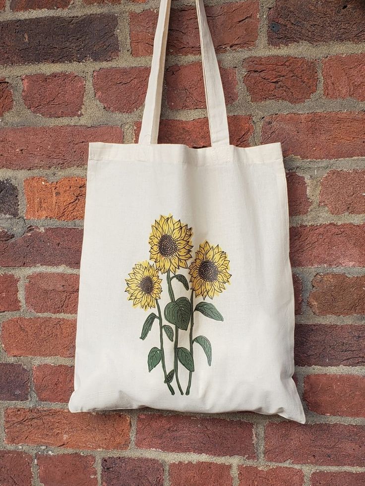 a white tote bag with sunflowers on it hanging from a brick wall