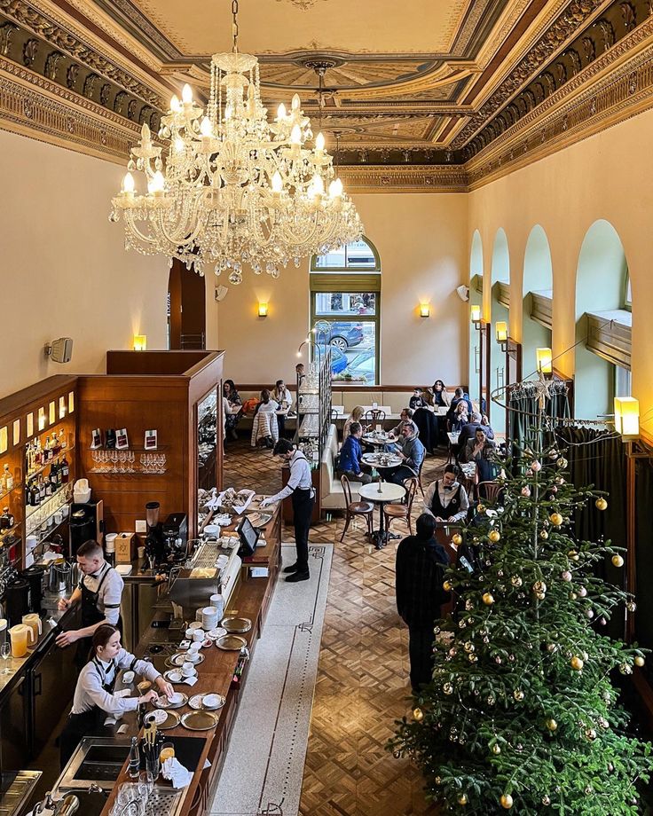 people sitting at tables in a restaurant with christmas trees and chandeliers hanging from the ceiling