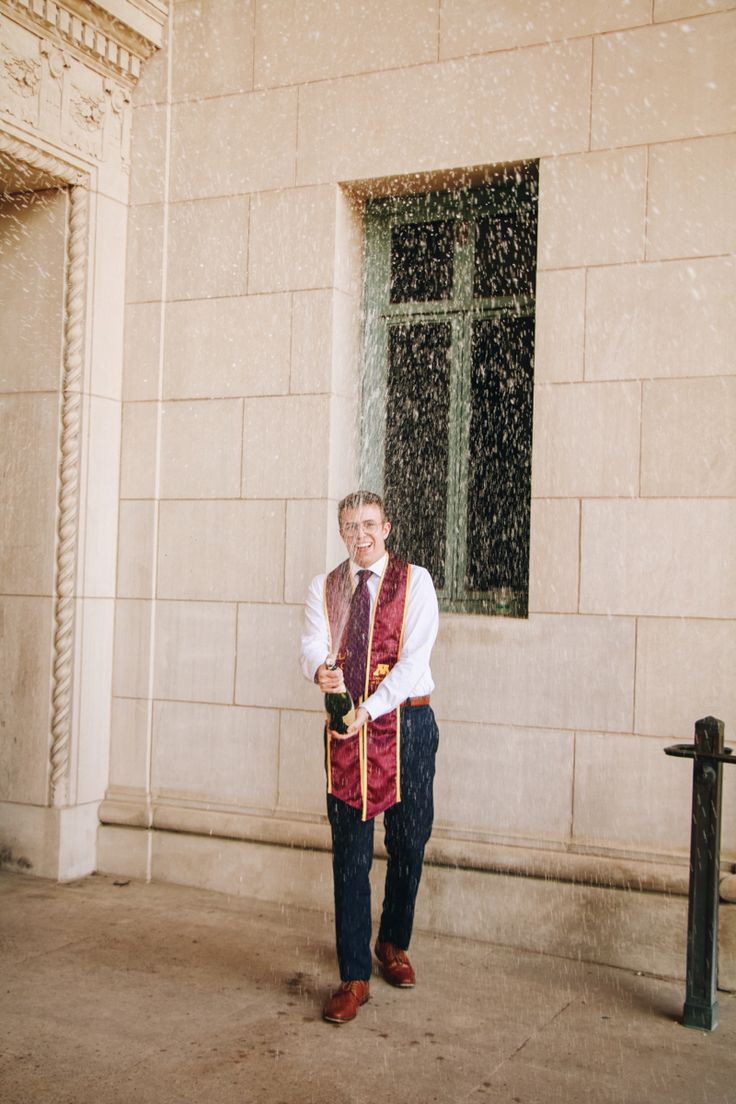 a man standing in front of a building wearing a red vest and tie with his hands on his hips