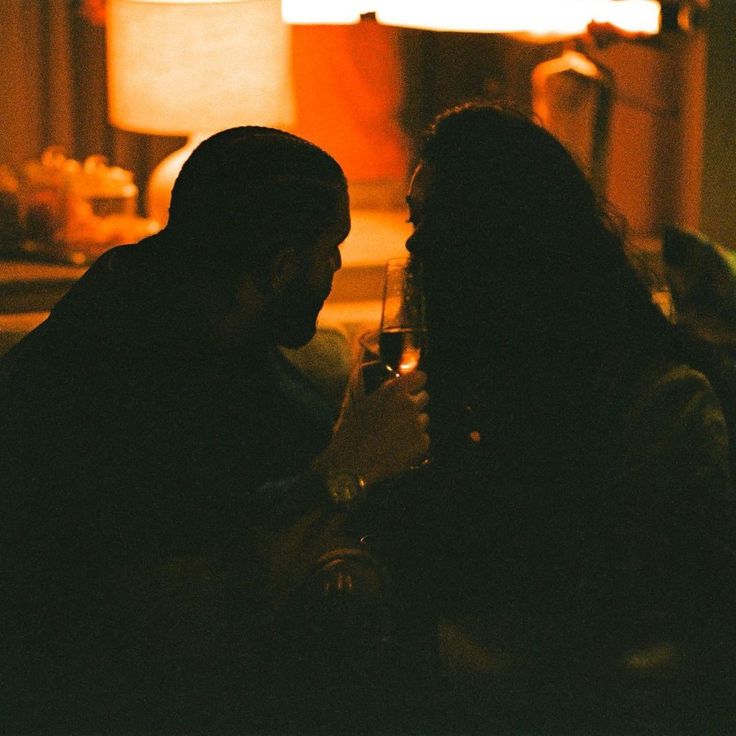 two people sitting next to each other holding wine glasses in front of a light that is on