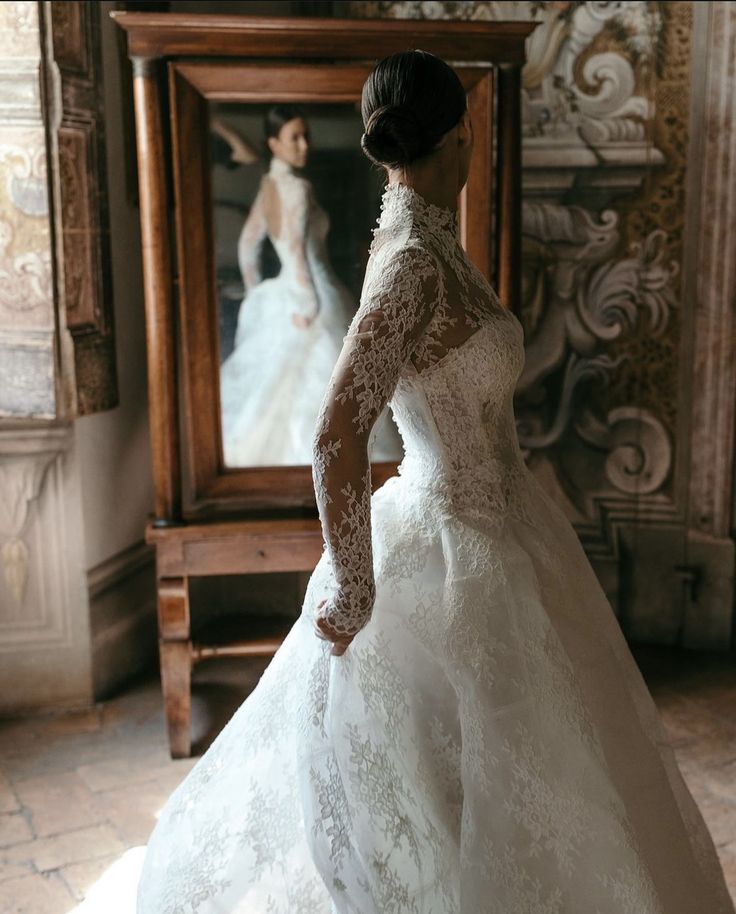 a woman in a white wedding dress looking at herself in the mirror with her hand on her hip