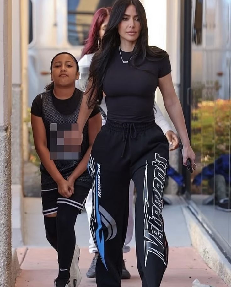 a woman walking down a sidewalk next to a little boy wearing black and blue pants