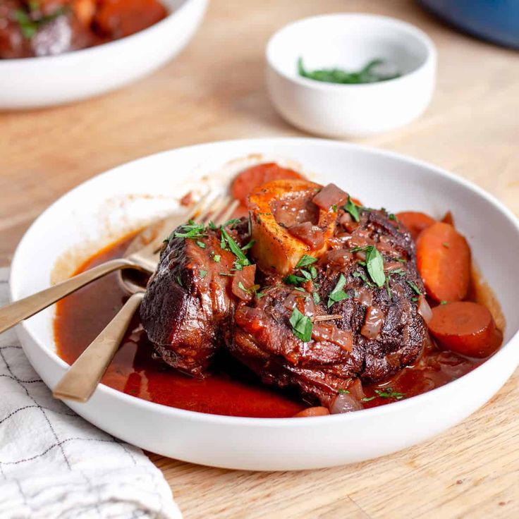 a white bowl filled with meat and carrots on top of a wooden cutting board