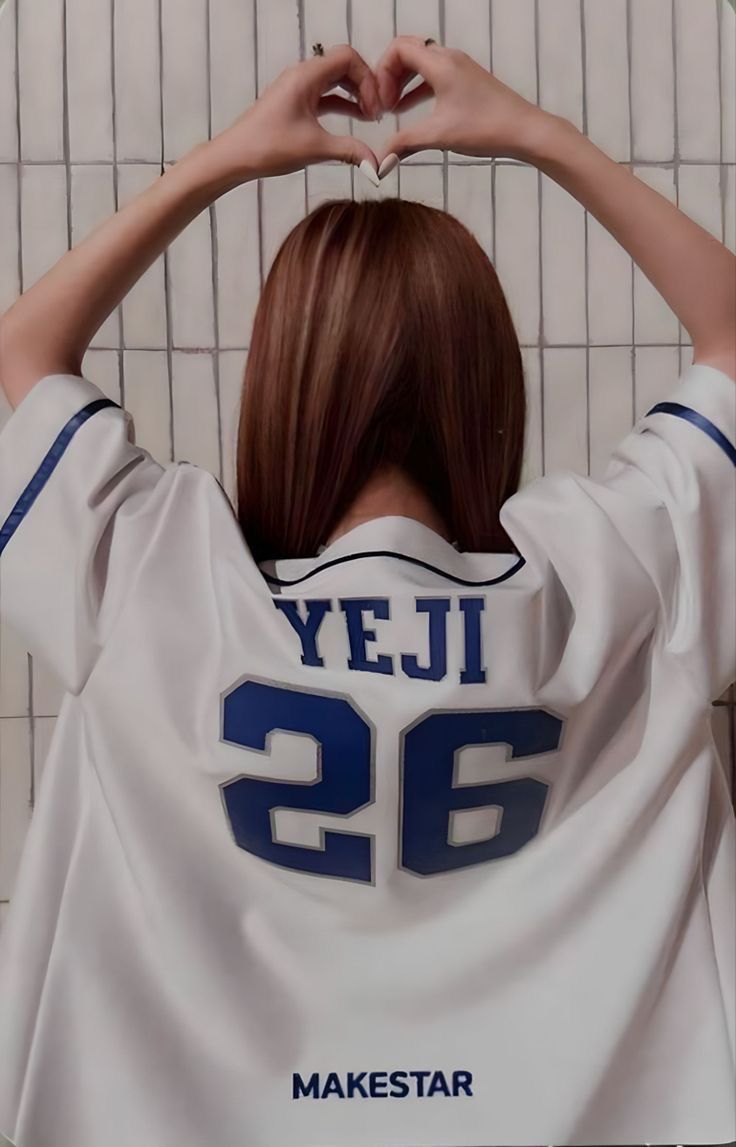 a woman in a baseball uniform making a heart with her hands