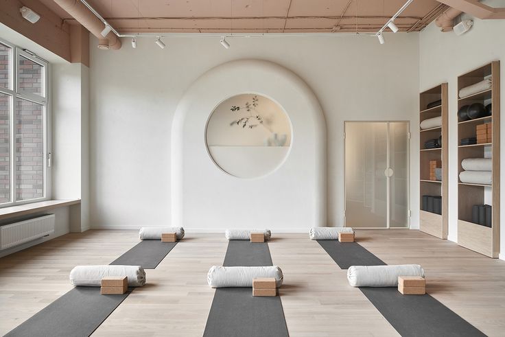 an empty yoga room with rolled up mats on the floor in front of a circular window