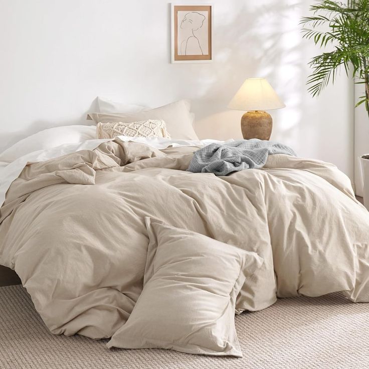 an unmade bed in a white bedroom with a potted plant on the side