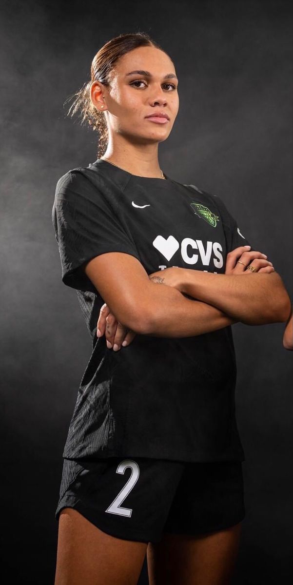 a female soccer player poses for a photo in her black uniform with her arms crossed