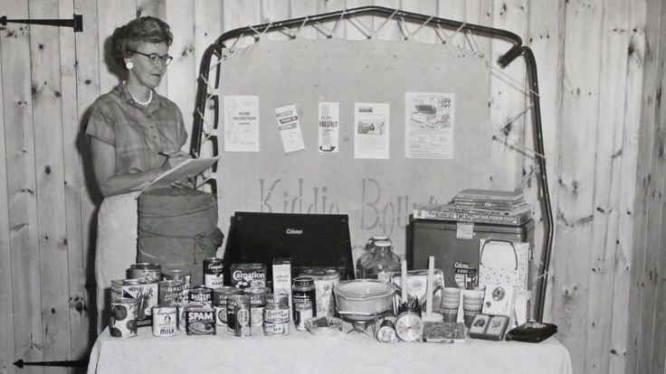 an old black and white photo of a woman standing in front of a table full of food