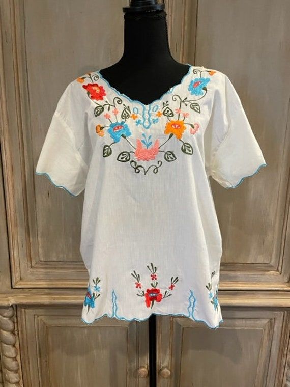 Cute Mexican embroidered top! Vibrant  flowers in orange, red and blue on a dark green vine surround the neckline and continue down the bodice. The same design can be found on the sleeves and edging the  bottom. The same areas have a turquoise embroidered edge. The size is estimated to be a ladies M.  The garment is in perfect condition, showing no signs of wear.  I do not make exchanges or accept returns.  Don't hesitate to contact me with questions! Multicolor V-neck Top With Floral Embroidery, Multicolor Embroidered Floral Print V-neck Top, Multicolor Floral Embroidered V-neck Top, Embroidered V-neck Festival Top, Traditional V-neck Top With Floral Embroidery, Short Sleeve Tops With Multicolor Embroidery And Embroidered Hem, Casual Multicolor Tops With Embroidered Sleeves, Folk Style V-neck Top With Embroidered Hem, Multicolor V-neck Blouse With Embroidered Neckline