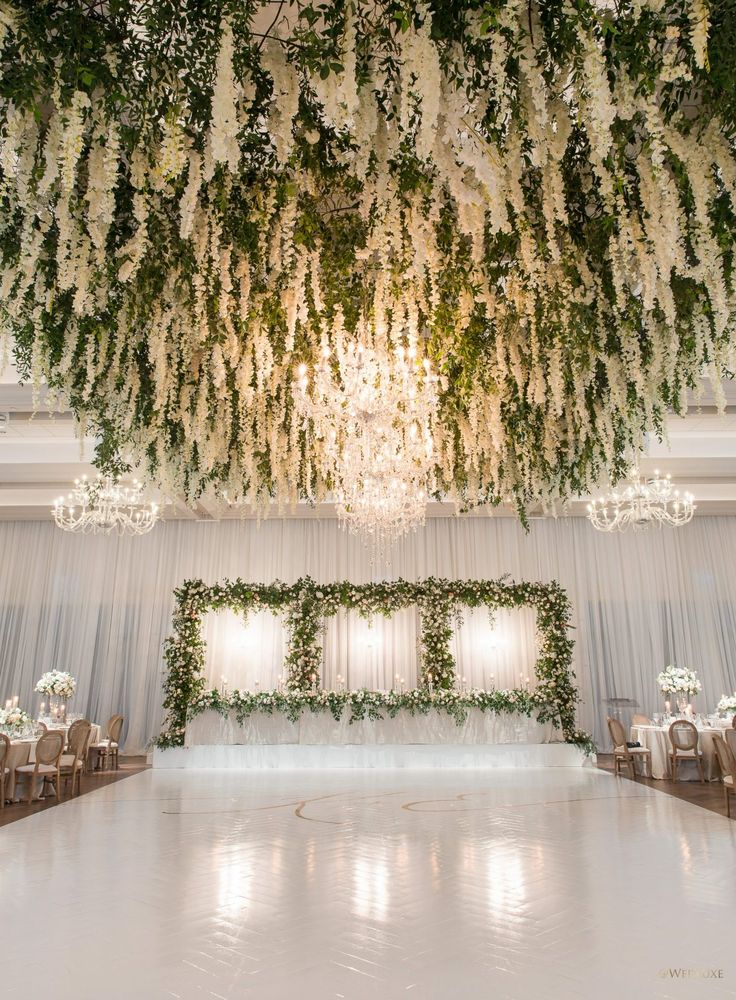 an elegant wedding setup with white flowers and greenery hanging from the ceiling, surrounded by chandeliers