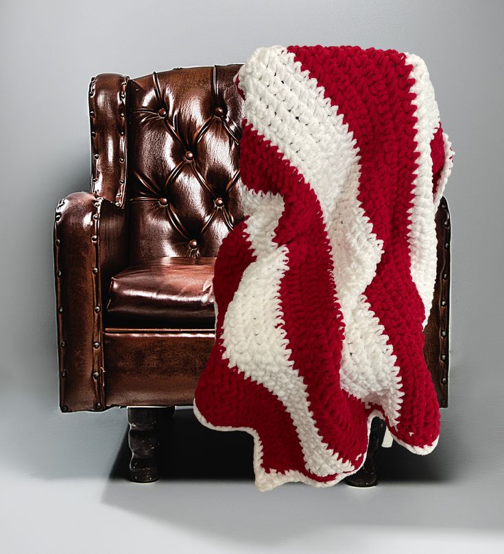 a red and white crocheted blanket sitting on top of a brown leather chair