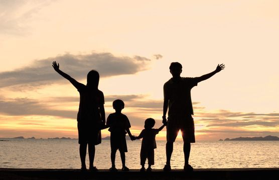 a family is standing on the beach at sunset with their arms up in the air