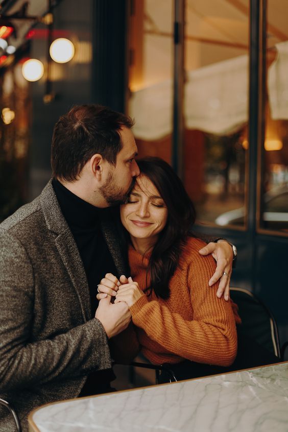 a man and woman hugging each other at a table in front of a restaurant window