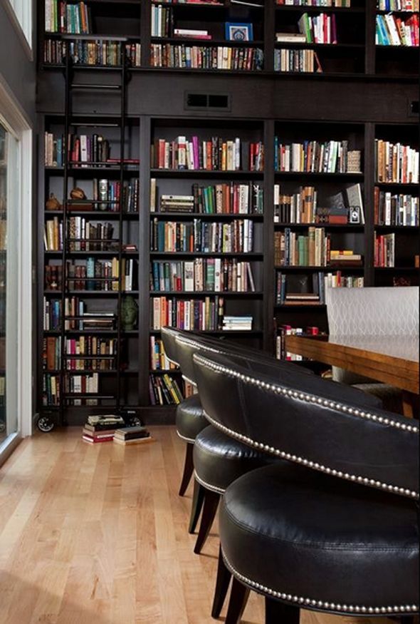 a room filled with lots of books next to a wooden table covered in black leather chairs