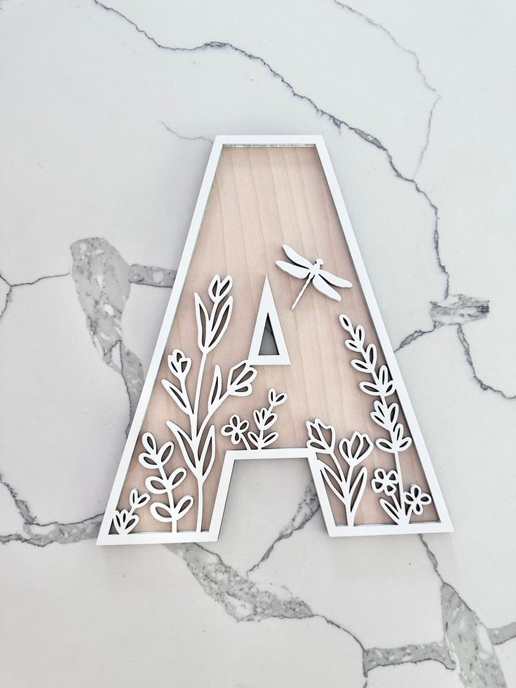 the letter a is cut out of wood with flowers and dragonflies