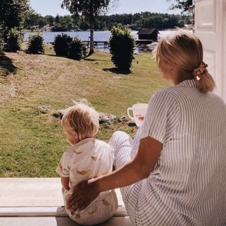 a woman sitting on the window sill holding a small child in her lap and looking out