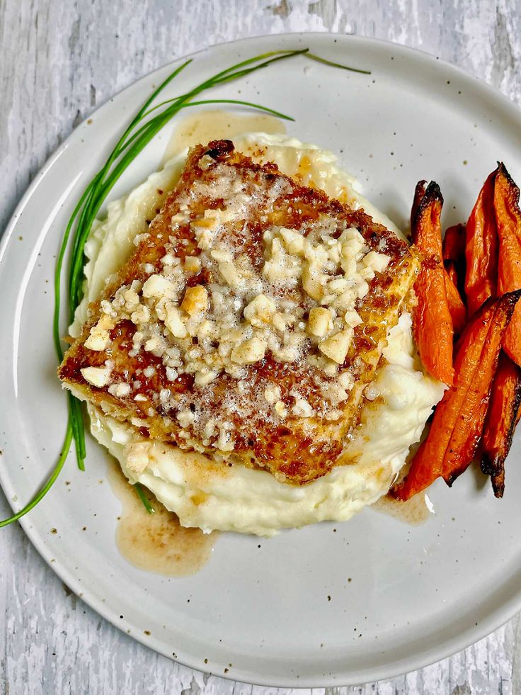 a white plate topped with mashed potatoes covered in sauce and garnished with chopped carrots