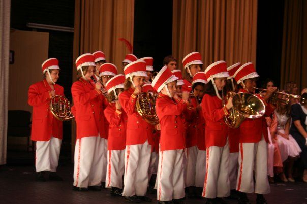 a group of children in red and white uniforms playing musical instruments while wearing santa hats