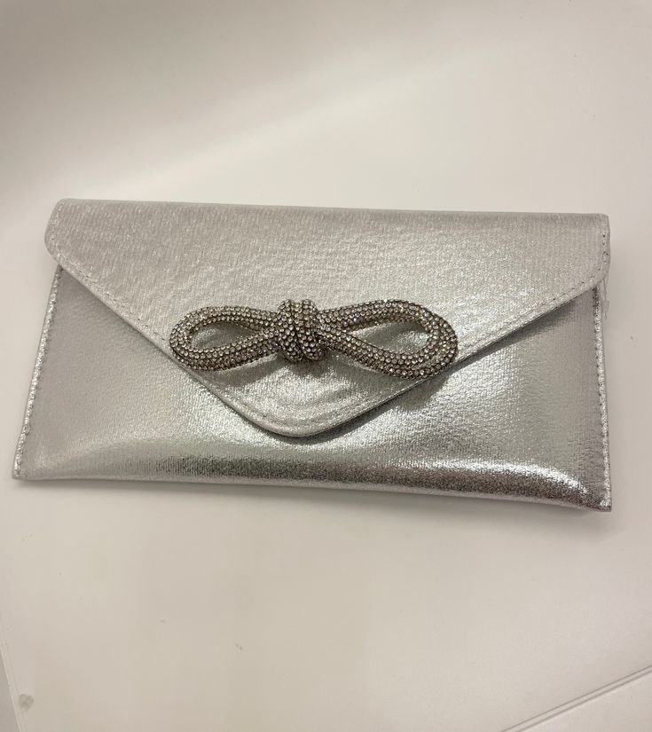 Look dazzling and stylish with this eye-catching Fancy Clutch with Bow. Not only will your outfit stand out, but you'll be sure to turn heads wherever you go! A must-have accessory for any event or occasion. Comes with a purse strap! Silver Glamorous Evening Bag For Party, Elegant Clutch For Party Season, Trendy Silver Clutch For Formal Occasions, Trendy Silver Evening Bag For Night Out, Trendy Silver Clutch For Night Out, Chic Silver Evening Bag For Party, Trendy Silver Clutch, Silver Evening Bag For Party Season Events, Chic Silver Clutch For Events