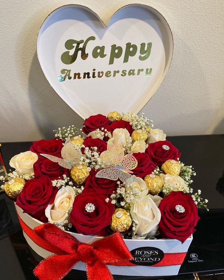 a bouquet of roses and chocolates in a heart shaped box with the words happy anniversary written on it