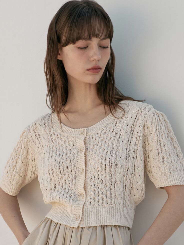 a woman wearing a white sweater and beige skirt standing in front of a wall with her hands on her hips