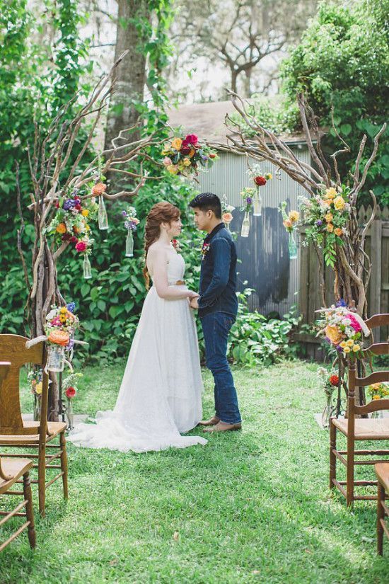 a man and woman standing next to each other in front of a wooden arch with flowers on it