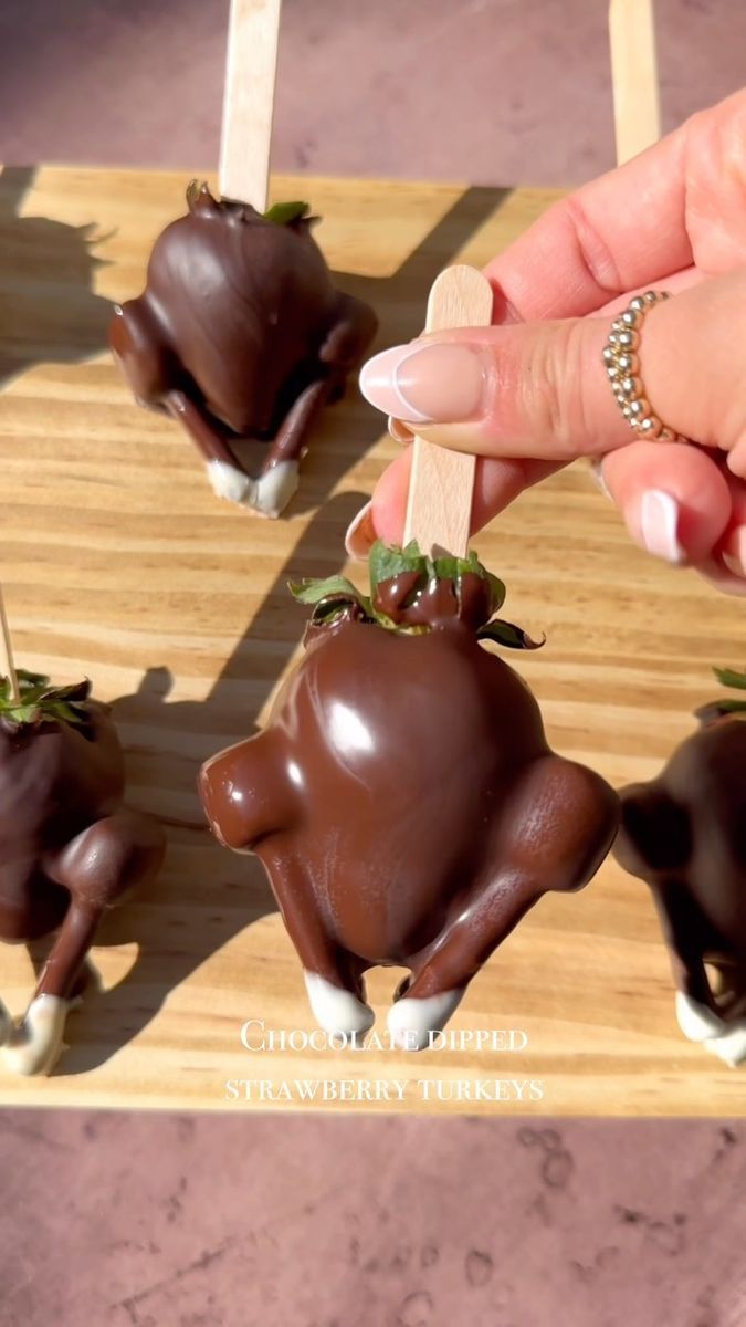 chocolate covered strawberries are being held up by someone's hand on a wooden tray