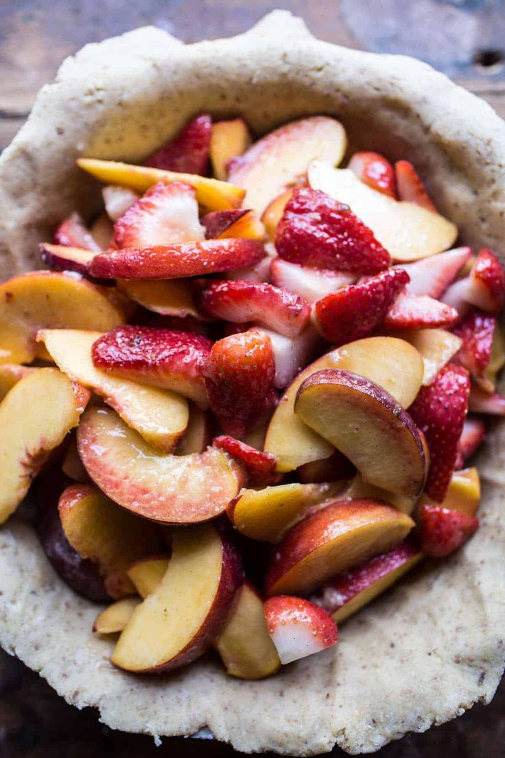 an uncooked pita filled with sliced apples and strawberries, on top of a wooden table