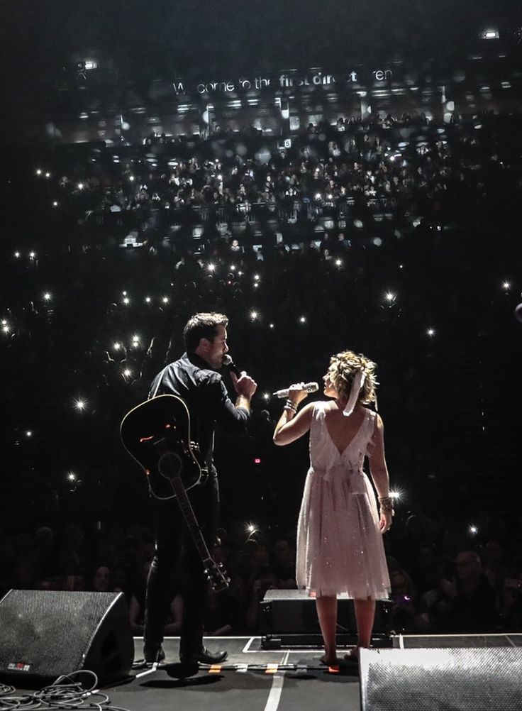 a man and woman singing on stage with lights in the background