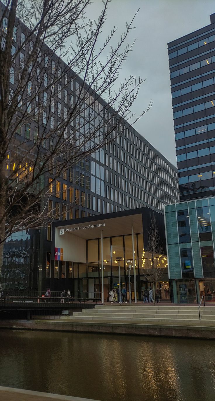 an office building next to a body of water in front of tall buildings at dusk