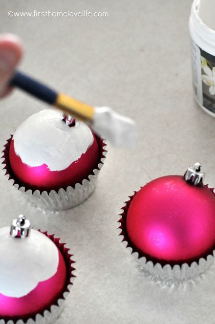 three red and white christmas ornaments being painted with acrylic paint next to a cupcake tin