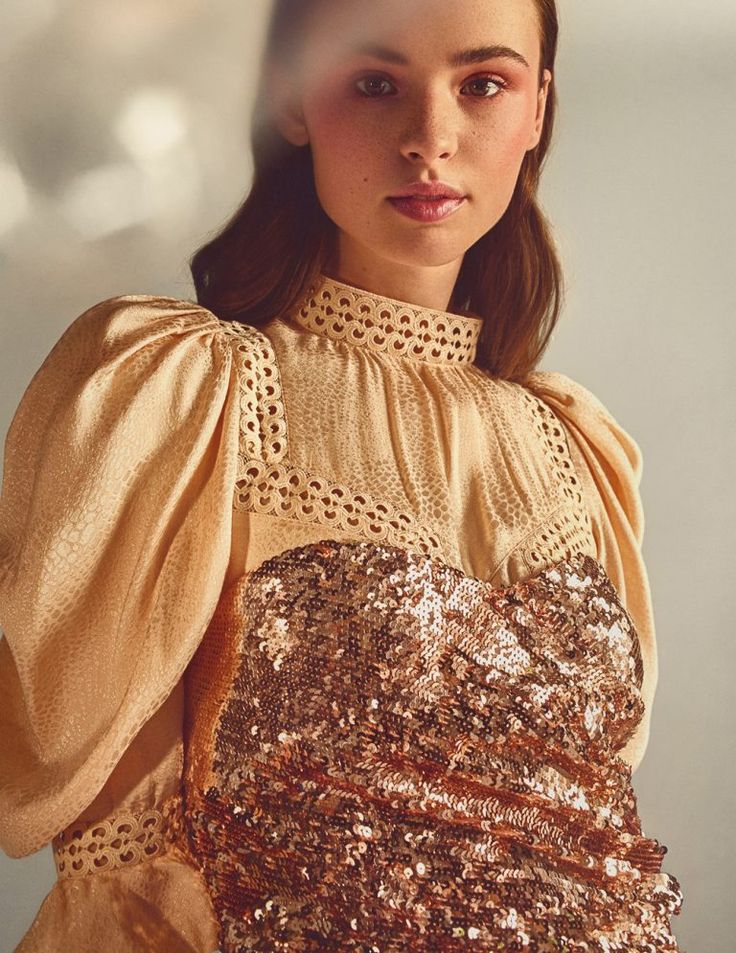 a woman with brown hair wearing a gold sequin dress and posing for the camera