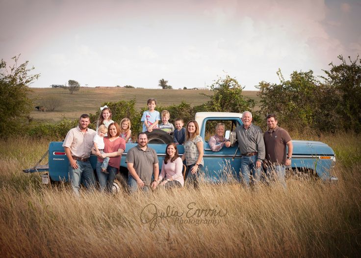 a group of people are posing in front of an old blue truck with the hood up