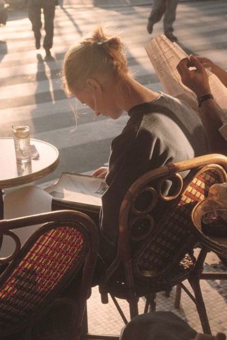 a woman is sitting at an outdoor table with her cell phone in her hand and people walking by