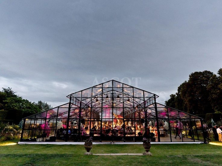 a large glass structure with people standing around it in the middle of a grassy area