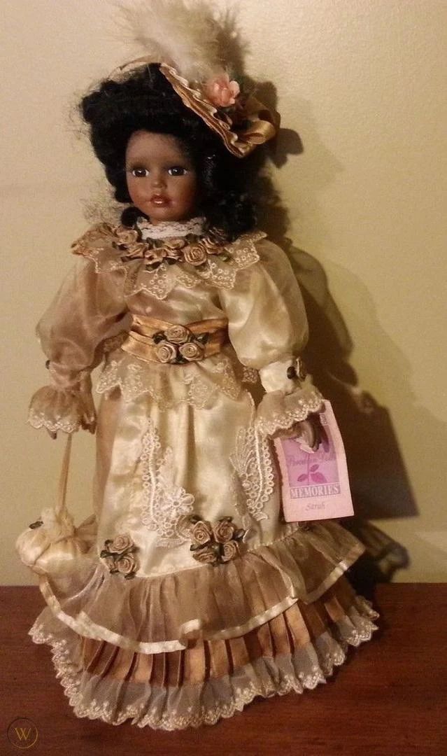 a doll is sitting on a table with a tag in it's hand and wearing a dress