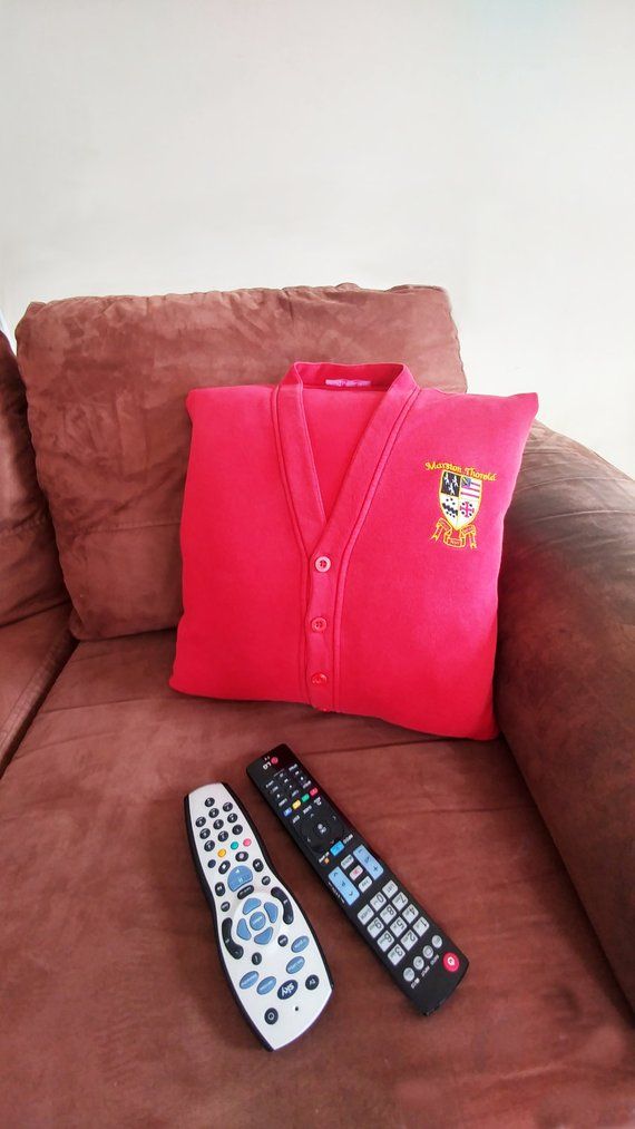 two remote controls and a pink pillow on a brown couch with a red sweater sitting on it