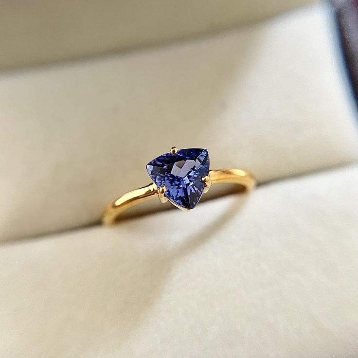 a tan and blue ring sitting on top of a white cloth covered box with a gold band