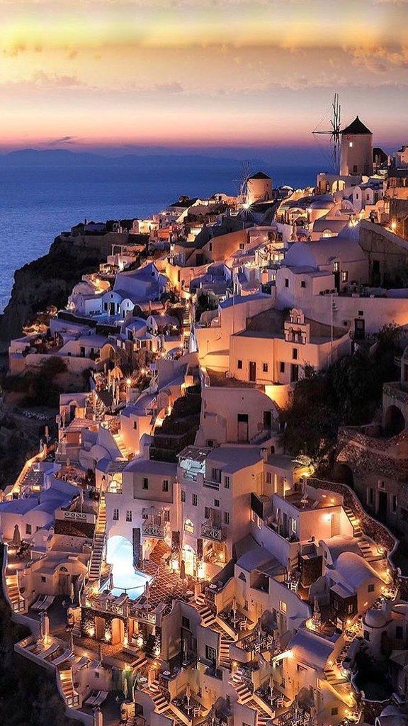 the town is lit up at night by the ocean with lights on its buildings and stairs