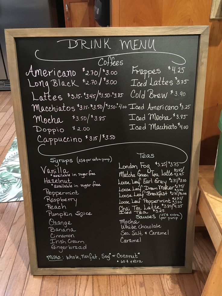 a blackboard with drinks and menus written on it in front of a wooden table