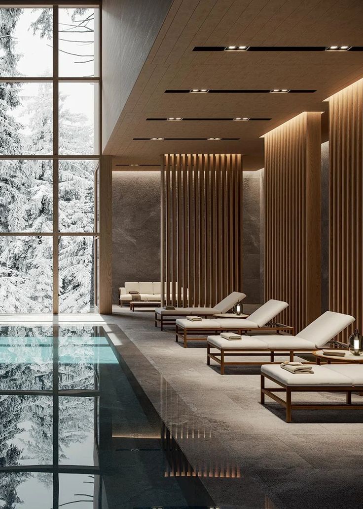 an indoor swimming pool with chaise lounges next to it and snow covered trees in the background