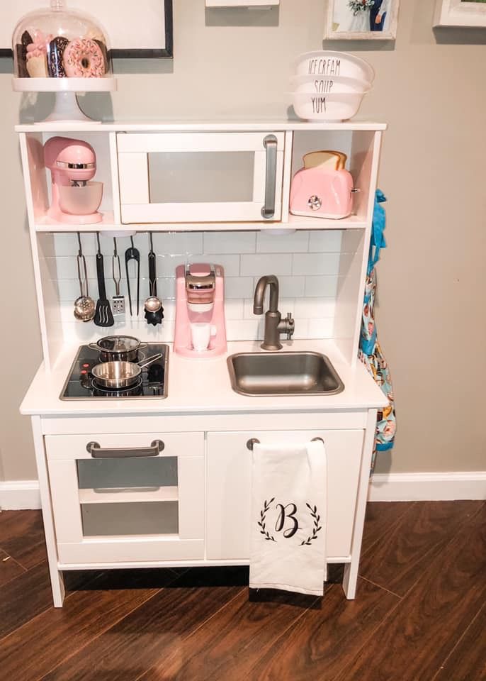 a toy kitchen with white cabinets and pink accessories