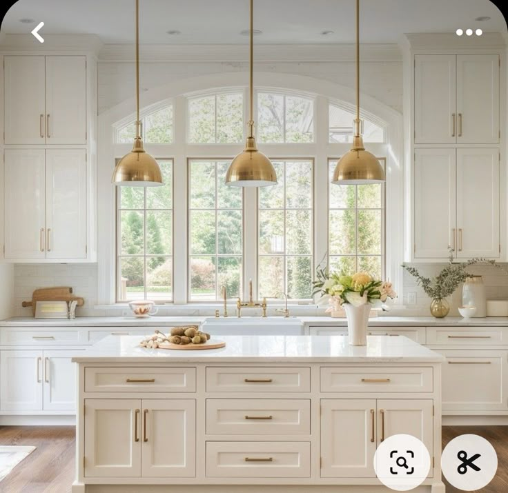 an image of a kitchen with white cabinets and gold pendant lights hanging over the island