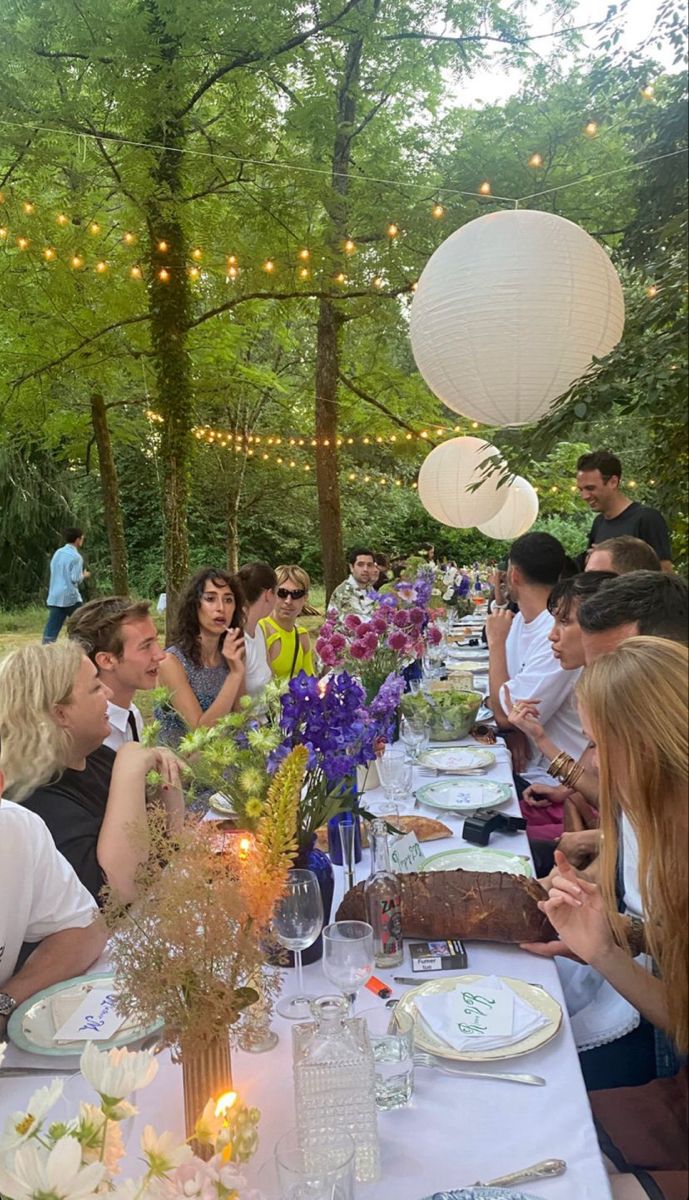 a group of people sitting at a long table with plates and flowers in front of them