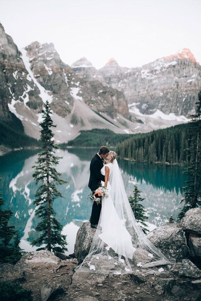 a bride and groom standing on top of a mountain next to a body of water