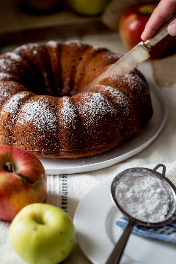 a person cutting into a bundt cake on top of a white plate next to apples