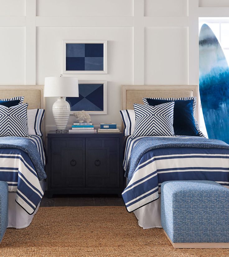 two beds with blue and white bedding in a bedroom next to a nightstand topped with a surfboard